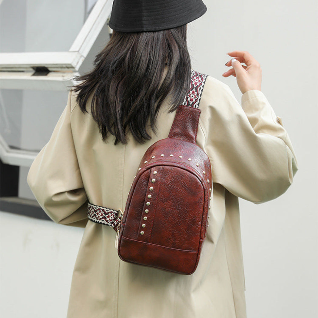 Person wearing a beige coat and black hat with a brown leather bag on a plain background